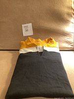 Folded men's long sleeve sweater showing the color block design in yellow, white, and gray.