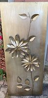 Large metal wall art piece with two flowers and stems mounted on a rectangular panel