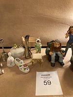 Miniature figures and doll house accessories arranged on a soft brown surface showing variety of items in lot