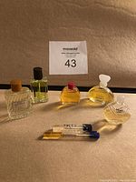 Full lot of five miniature perfume bottles and two sample vials arranged on beige background.
