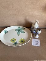 Photo showing oval Johnson Brothers plate with floral pattern, ceramic hand pump, and candleholder.