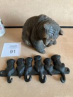 Photo showing terra-cotta bear figurine sitting and cast iron puppy dog hook set side by side.