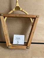 Full view of racket in trapezoidal wooden holder with metal screws.