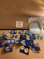 Multiple sets of vintage earrings on blue and silver cards along with a gold tone chain necklace on a brown surface.