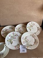 Five floral patterned plates arranged in fan shape on beige surface with one tea cup on lower left corner.