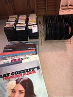 Photo showing vinyl LP albums including Ray Conniff's Hawaiian Album, 45 RPM singles in black holders, and 8-track tapes in rack.