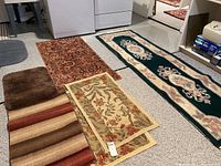 Six area rugs laid out on basement floor showing different patterns and sizes including runners and bath rug.