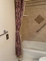 Photo of bathtub with beige tiled surround and outer shower curtain tied back, showing the bathroom space.