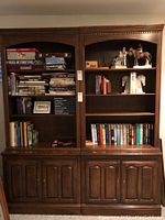 Overview of wooden bookcase with two sections showing board games, books, a few figurines, decanters, and an airplane picture