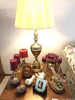 Photo showing brass lamp on wooden side table with six red candles in brass holders, two bird figurines, drink coasters in wooden holder, and small photo frame