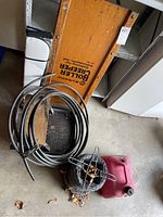 Overall view showing wooden creeper, black tubing coil, twisted wire bale and gas can on garage floor.