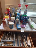 Photo of countertop with various household cleaning supplies including bottles, sprays, and powder containers.