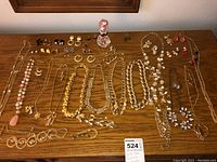 Top-view photo showing multiple gold tone necklaces with bead and chain designs laid flat on wooden surface alongside various matching earrings and bracelets.