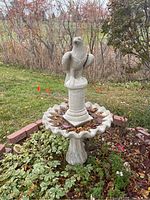 Overall view of the complete concrete bird bath outdoors in a garden setting showing eagle atop, scalloped basin and leafy surroundings.