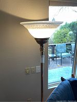 Full view of the floor lamp showing the white frosted glass shade and the top portion of the brass pole.