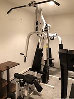 Front and side view of Pacific Fitness home gym machine featuring seat, pulldown bar, and leg curl attachment.