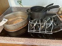 Cookware and bakeware items on stovetop including aluminum roasting pan, non-stick pans, and glass lids on drying rack