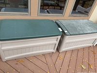 Photo showing two large plastic outdoor storage boxes with beige bases and green lids on deck flooring.