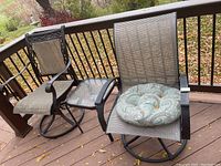 Two black metal patio swivel chairs with tan mesh seats and backs with patterned seat cushions, next to a small square glass-top side table with black metal legs, taken on patio deck.