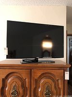 Front view of the Samsung TV on a wooden cabinet, showing the full front screen and part of the stand.