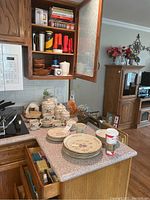 Overview of kitchen countertop and open cabinet with stoneware dishes, mugs, flashlights, and other kitchen items visible.