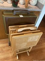 View showing both sets of TV trays leaning against the counter, with emphasis on the wooden trays and their wooden folding caddy in front.