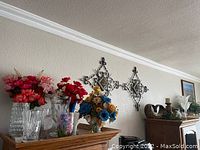 View of metal wall decor, vases, and faux flowers arranged on wood furniture.
