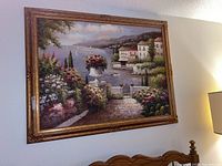 Full view of the framed oil painting showing a coastal village scene with flowers, water, and sailboats.