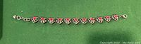 Photo showing 925 silver heart bracelet with red enamel hearts on green background, clasp and small heart charm visible.