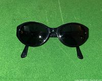 Front view of black oval-shaped Emporio Armani sunglasses on green background.