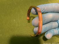 Men's bracelet held by a gloved hand showing rose gold and yellow gold electroplated stripes on cuff style open bracelet.