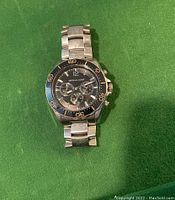 Front view of silver-tone men's wristwatch with black dial and chronograph subdials on green background