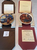 Both plates presented in original boxes with certificates of authenticity visible and resting on packaging material.