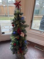 Full view of the 4 foot artificial Christmas tree decorated with red berries, red ball ornaments, and a bird with gold accents, lit with multi-color lights.