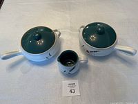 Set of three Denby Oven Proof kitchen wares: small pitcher and two covered casseroles, all with dark green lids and handles, white bases decorated with a botanical wheat and grass motif.