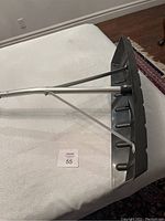 Snow rake head with black plastic and metal supports lying on white fabric background.