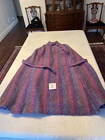 Full view of the wool cape showing purple, blue and grey vertical stripes, displayed flat with the belt and label visible.