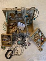 Overall view of vintage embroidered jewelry box open, showing interior mirror and multiple fashion jewelry pieces including necklaces, bracelets, earrings, and brooches.