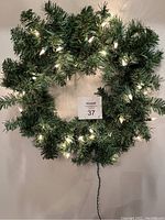 Photo of a green artificial Christmas wreath with white lights turned on, wall-mounted, 20 inches diameter