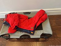 Full view of foldable cooling pet bed with red Muttluks dog snowsuit laid on top.