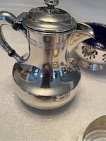 Front view of a silver plate sauce server with lid and handle, showing its reflective polished surface.