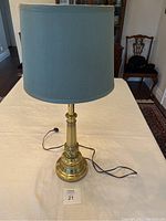 Full view of brass table lamp with shade on display with power cord visible.