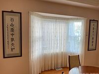 Wide view showing both framed Asian calligraphy scroll artworks hanging on wall beside window with curtains.