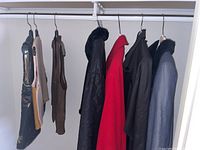 Full view of coats and vests hanging in closet, showing four coats and three vests of various colors and styles