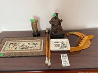 Full lot view showing all five items on a table including bronze figurine, ceramic tray, wooden decor, Asian mat, and horn vase.