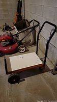 Photo of entire dolly showing orange metal frame, white wood platform, two large rear wheels, and handle.