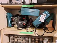 Shelf with several blue-colored power tools including cordless drill, jigsaw, and charger shows the range of tools in the lot.