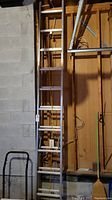 Full view of the aluminum extension ladder vertically positioned against a wall in a garage setting, displaying the full length and rung spacing.