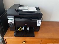 Front view of HP LaserJet 100 Color MFP M175nw showing control panel, paper tray, and included manual and CD on top.