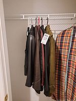 Photo of several leather outerwear pieces hanging together including coats and jackets on a rack.